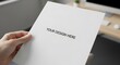 © Top_Stock - Hand holding a blank white A4 paper mockup against a blurred office desk background. Template for flyer, resume, or document presentation.