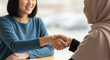 © Su Young Moon - Close-up of two businesswoman sitting at a table shaking hands.