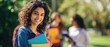 © Inna - The smiling student holding colorful folders in a sunny outdoor campus setting.