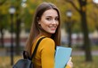 © ENDRA - A smiling young woman, possibly a student, holding books and a backpack outdoors in an autumn park setting, looking over her shoulder