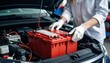 © Kaifiya - Professional mechanic installing a new red car battery under the hood in a service center.