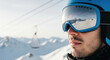 © Bakha - Confident man wearing blue ski helmet and reflective goggles stands in snowy mountain landscape with cable cars and bright clear winter sky in background