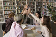 © fizkes - Team support for education success. Excited international group high school students join hands in high five at study desk celebrate finishing joint academic project united by friendship shared goals