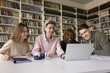 © fizkes - Collaborative remote studying. Group of 4 smiling motivated multicultural young people college university students meet at library desk to watch video lecture on online education platform via notebook