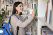 © fizkes - Love for traditional reading. Smiling teen girl university student buy printed books at store choose paper editions of scientific literature at campus library to prepare for lecture research project