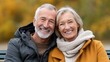 © Luvencia - A joyful older couple sitting together, smiling warmly, surrounded by autumn colors, showcasing love and companionship.