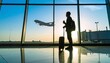 © IKetut - Silhouette of a traveler with luggage in an airport terminal, watching an airplane take off at sunrise. Concept of a journey, departure, and business travel.