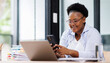 © David - African black business woman using smartphone while working on laptop at office. african american businesswoman looking up while working on phone. Successful woman entrepreneur.