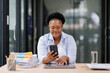 © David - African black business woman using smartphone while working on laptop at office. african american businesswoman looking up while working on phone. Successful woman entrepreneur.