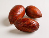 Three fresh salak fruits with reddish-brown scaly skin, arranged on a clean white surface in soft natural light.