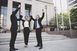 © khwanchai - Business investors in suits stand with their hands raised in celebration after achieving their goals outside an office building.