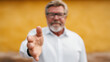 © Chaiwit - Friendly senior man extending hand for handshake with warm yellow background, inviting connection and trust in casual setting