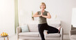 © Prostock-studio - Domestic yoga practice. Positive mature lady standing in tree pose, keeping balanced during covid lockdown at home. Happy senior lady in sportswear exercising indoors, copy space