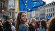 © Maryna - Crowded city street with people holding flags. Woman smiles with European flag, blue, yellow, yellow stars in hands. Diverse crowd, flags, cityscape, building, lamppost, tree. Low-angle shot