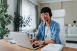 © Miljan Živković - Asian freelancer woman working from home having video call on laptop