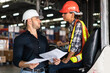 © winnievinzence - Warehouse supervisor and female forklift operator reviewing documents. Concept of teamwork, training, and logistics management in an industrial environment