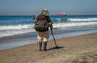 © F Armstrong Photo - A man using a metal detector on a beach with the ocean and waves in the background
