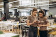 © Roman - Two Women Discussing An Order on a Smartphone in a Furniture Store