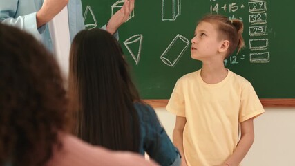 Poster - Professional teacher talking and explain idea to asian child during class. Caucasian student listening instructor while standing in front of classroom with blackboard math lesson written. Pedagogy.