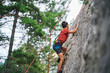 © Marc Elias - Young boy climbing rock wall with rope in forest environment