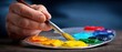 © Sonthana - A hand holding a brush paints vibrant colors from a palette, showcasing creativity and the art of painting.