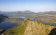 © Travel 'n' Lifestyle - View of jagged peaks descend to a tapestry of blue waters and verdant wetlands under a clear sky, Lofoten, Leknes, Nordland, Norway.