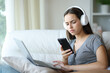 © PheelingsMedia - Confused woman checking phone while is using laptop