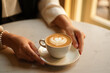 © MstEva - Woman enjoying a delicious latte with heart shaped foam art in a bright cafe setting perfect for a coffee break