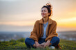 © EricMiguel - Young woman meditating outdoors at sunset, enjoying peace and mindfulness while sitting cross-legged on grass