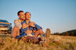 © we.bond.creations - Young couple enjoying a romantic moment during a road trip, embracing in a field at sunset near their parked car