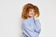 © SHOTPRIME STUDIO - smiling woman with curly hair in a blue sweater, light background, expressing happiness and warmth, showcasing casual and cozy style, ideal for lifestyle and fashion themes