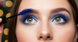 © helga - Woman applying vibrant blue mascara and eyeshadow for a bold, trendy eye makeup look, highlighting beauty and cosmetic application.