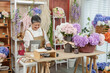 © Ekkasit A Siam - Asian senior florist smiling while using digital tablet in flower shop, surrounded by hydrangeas, showing joyful expression and active lifestyle as small business owner in retirement