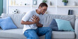 © Prostock-studio - Millennial African American guy having heart attack, touching his chest in pain, sitting on sofa at home. Young black man suffering from cardiovascular ache, getting infarction indoors