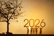© Creativa Images - Silhouette of people holding up the year 2026 at a beautiful sunset.