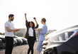 © sofiko14 - A woman celebrating a car purchase, holding keys, next to a car, with a salesperson and another man.