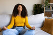 © Daniel - Front view of relaxed Black woman meditating on the sofa. Copy space.