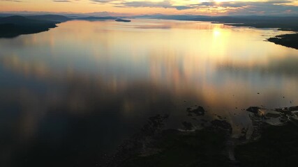 Wall Mural - calm lake reflecting a golden-pink sunset sky with distant hills and scattered clouds on the horizon