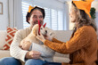 © Wavebreak Media - Couple styling puppy with red devil-horn headband on sofa while wearing Halloween bucket hats