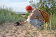 © DimaBerlin - Frightened anxious scowling leashed cat refuses approaching owner fearing beach walk. Man reassures feline for stroll, outdoor walk, hesitant pet owner patience, building trust with fearful animal