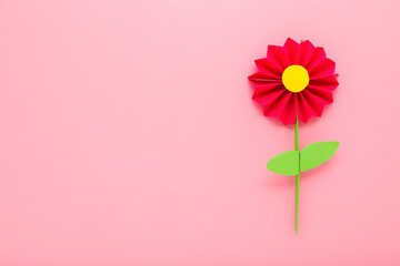 Wall Mural - Red flower with green leaves created from colorful application paper on light pink table background. Pastel color. Closeup. Empty place for text. Top down view.