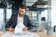 © Liubomir - A businessman is working in his modern office, reviewing documents and using his laptop. Focused and professional, he's dressed in a suit.