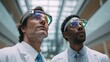 © Prapan - Technological Visionaries: Two scientists in lab coats gaze upward, wearing futuristic augmented reality glasses in a well-lit, modern setting.