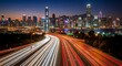 © Dinar - Long exposure captures streaks of car lights on highway leading to illuminated cityscape.
