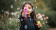 © GFX Corner - A cute little girl is playing with a bubble gun and making bubbles in a park on a sunny day