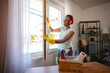 © Jelena - Smiling housekeeper opening window while listening to music with headphones