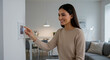 © Iuliia - Woman pointing on digital thermostat with screen display set at 23 degrees Celsius. Temperature regulator on wall within modern living room. Smart home climate control regulation. Selective focus