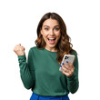 © YUSUF - Cheerful woman portrait showing a victory gesture after winning online, an ecstatic moment with her mobile phone, Isolated on a Transparent Background PNG.