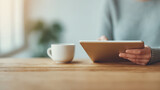 A person sits at a wooden table, holding a tablet with a coffee cup nearby, enjoying a cozy, productive moment.