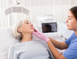 © JackF - Positive aged woman patient lying on clinical chair discussing face aesthetic procedures with a specialist